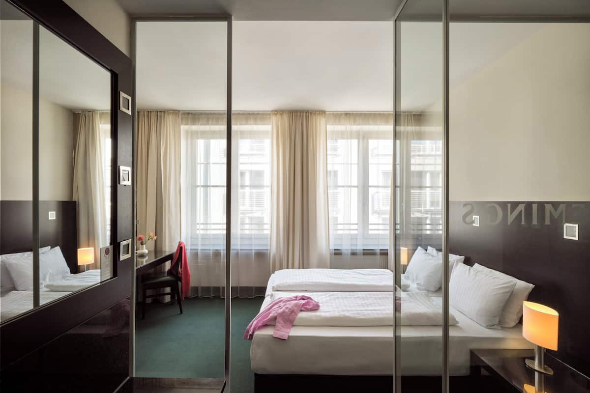 A hotel room with two beds, a large mirror, and a view of the city through large windows.