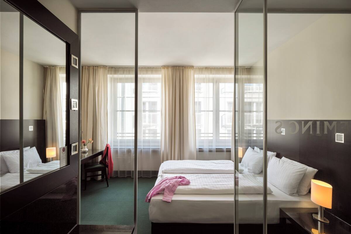 A hotel room with two beds, a large mirror, and a view of the city through large windows.