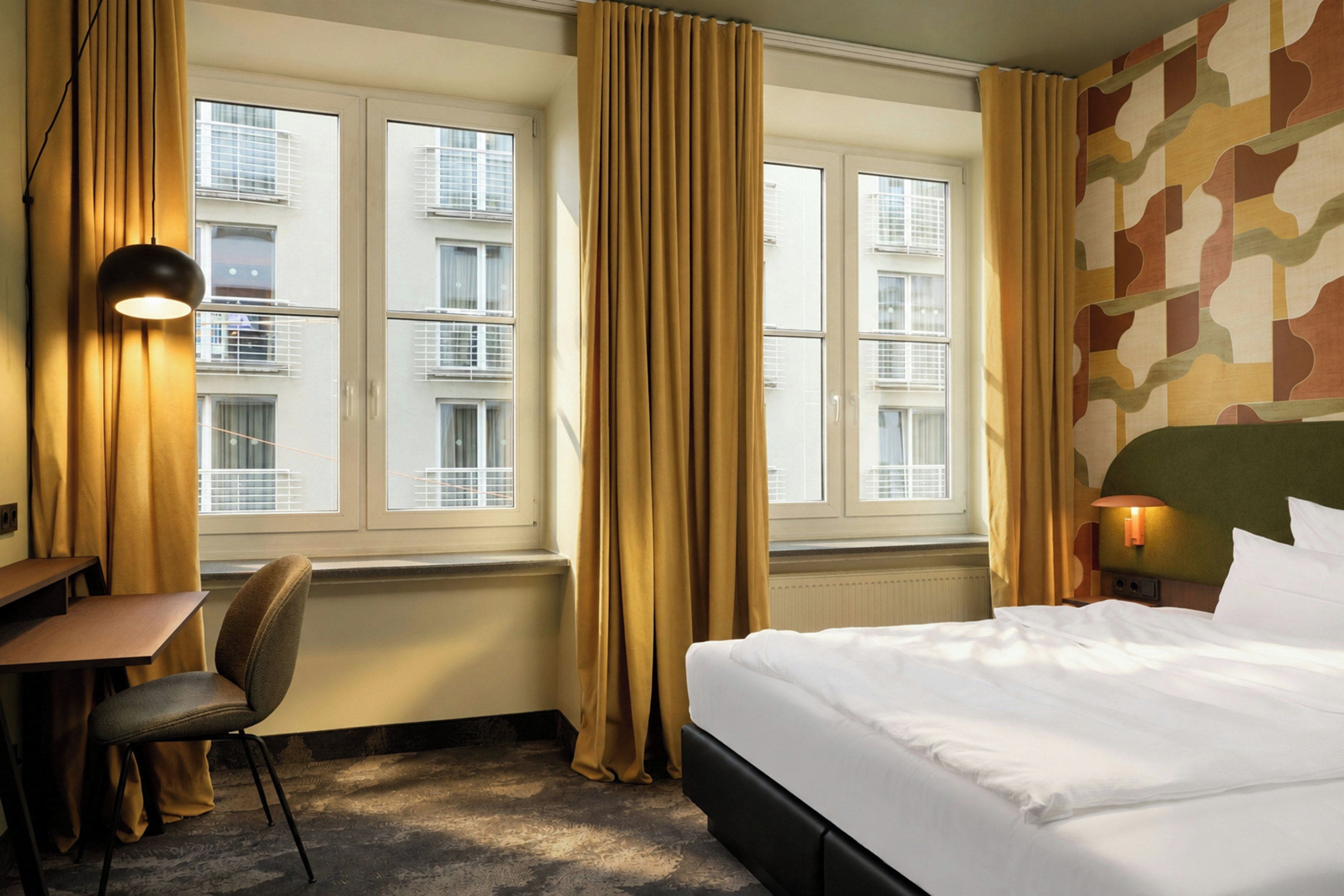 Een hotelkamer met een bed, een bureau, een stoel, een lamp en gordijnen.