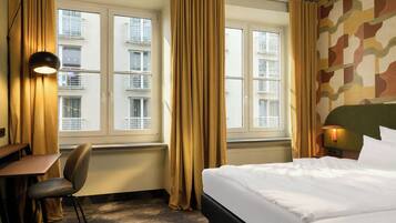 Een hotelkamer met een bed, een bureau, een stoel, een lamp en gordijnen.