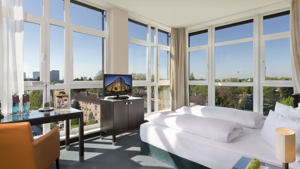 Una habitación de hotel con una cama grande, un escritorio, un televisor y vistas a la ciudad.