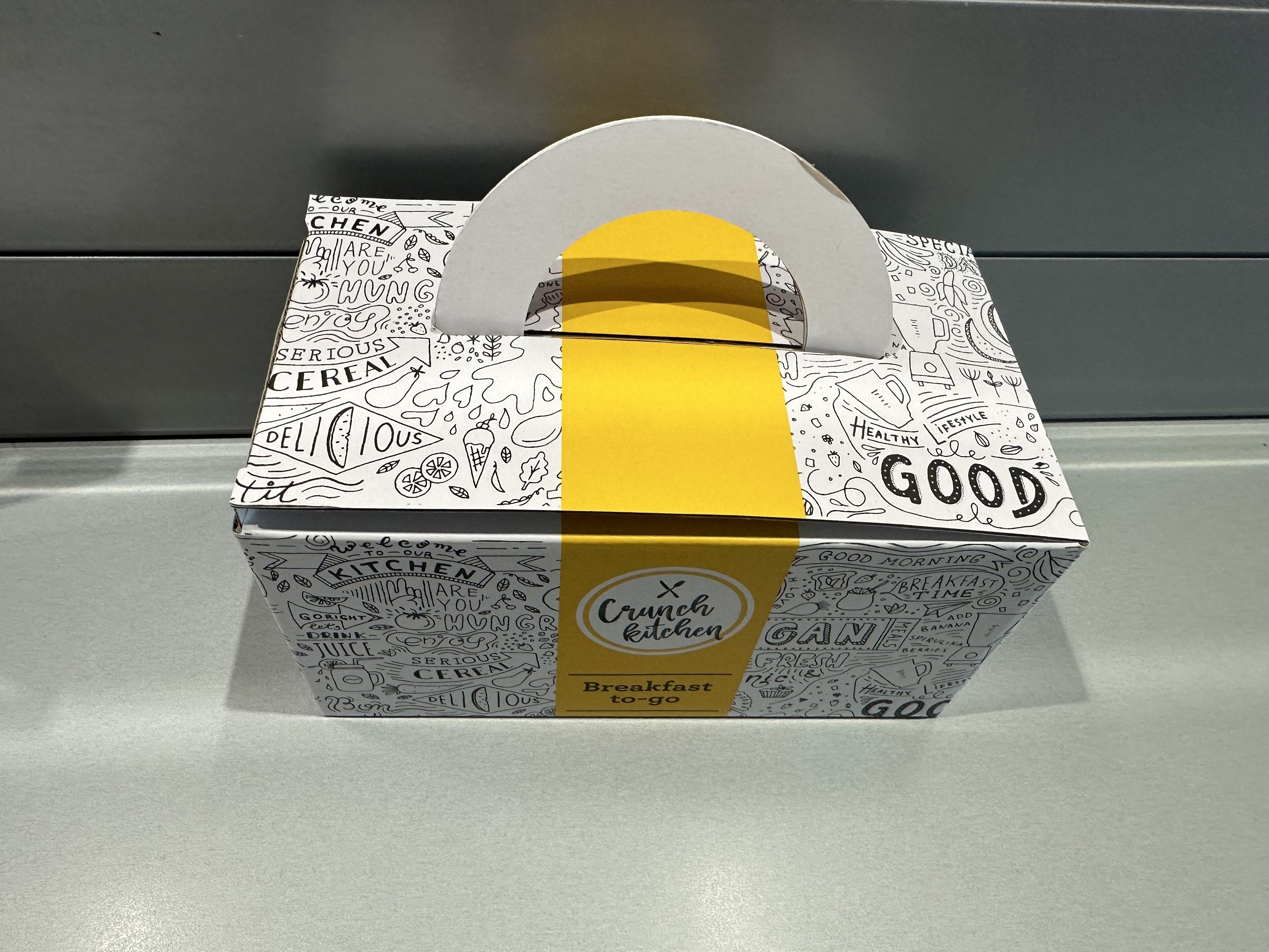 A box with a handle, decorated with doodles and text, including "Crunch Kitchen" and "Breakfast to go".