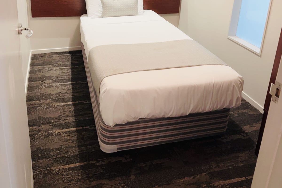A hotel room with a bed, a headboard, a framed picture on the wall, and a window.