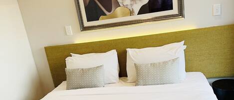 A neatly made bed with a patterned bedspread, two pillows, and a framed artwork above it.