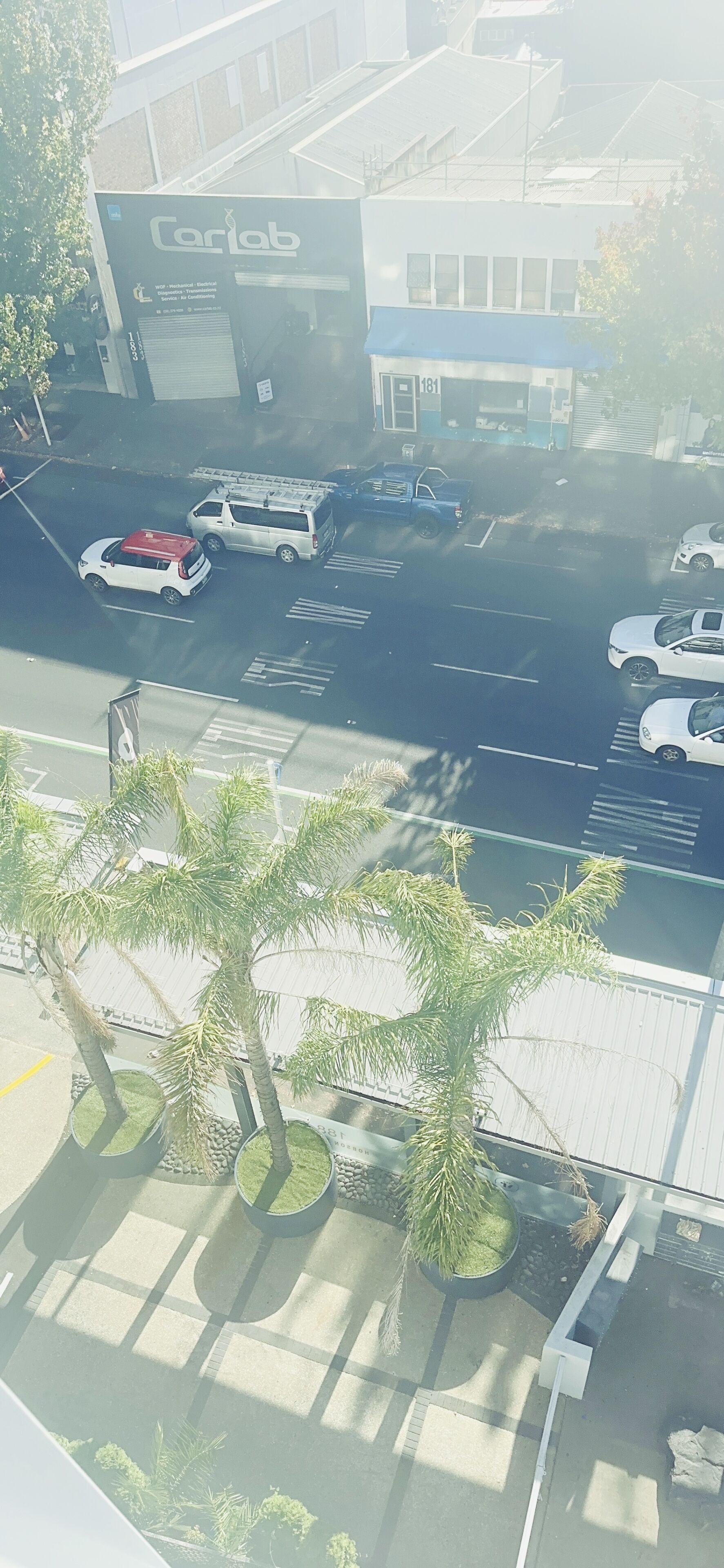 Un estacionamiento con varios coches, un edificio con un letrero que dice "Coriolab" y palmeras al frente.