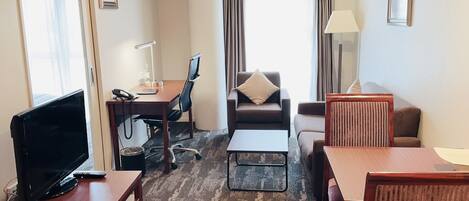 A hotel room with a TV, desk, chair, sofa, and a small table.