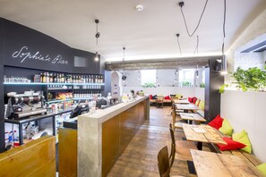 A bar area with a neon sign, wooden tables, and seating with red and green cushions. - Sophie's Hostel (Prague)