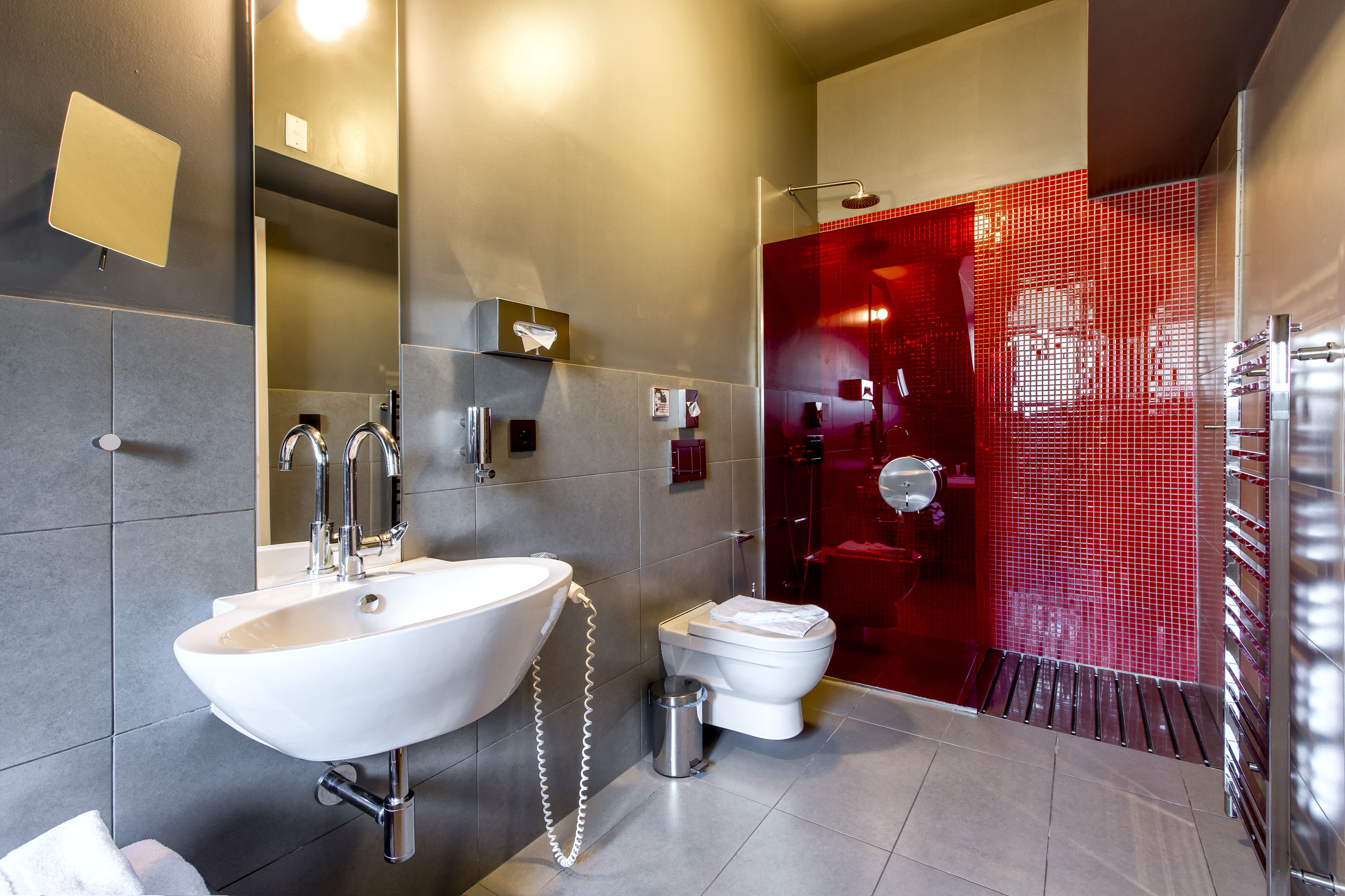 A modern bathroom with a large white sink, a toilet, and a red-tiled shower area.