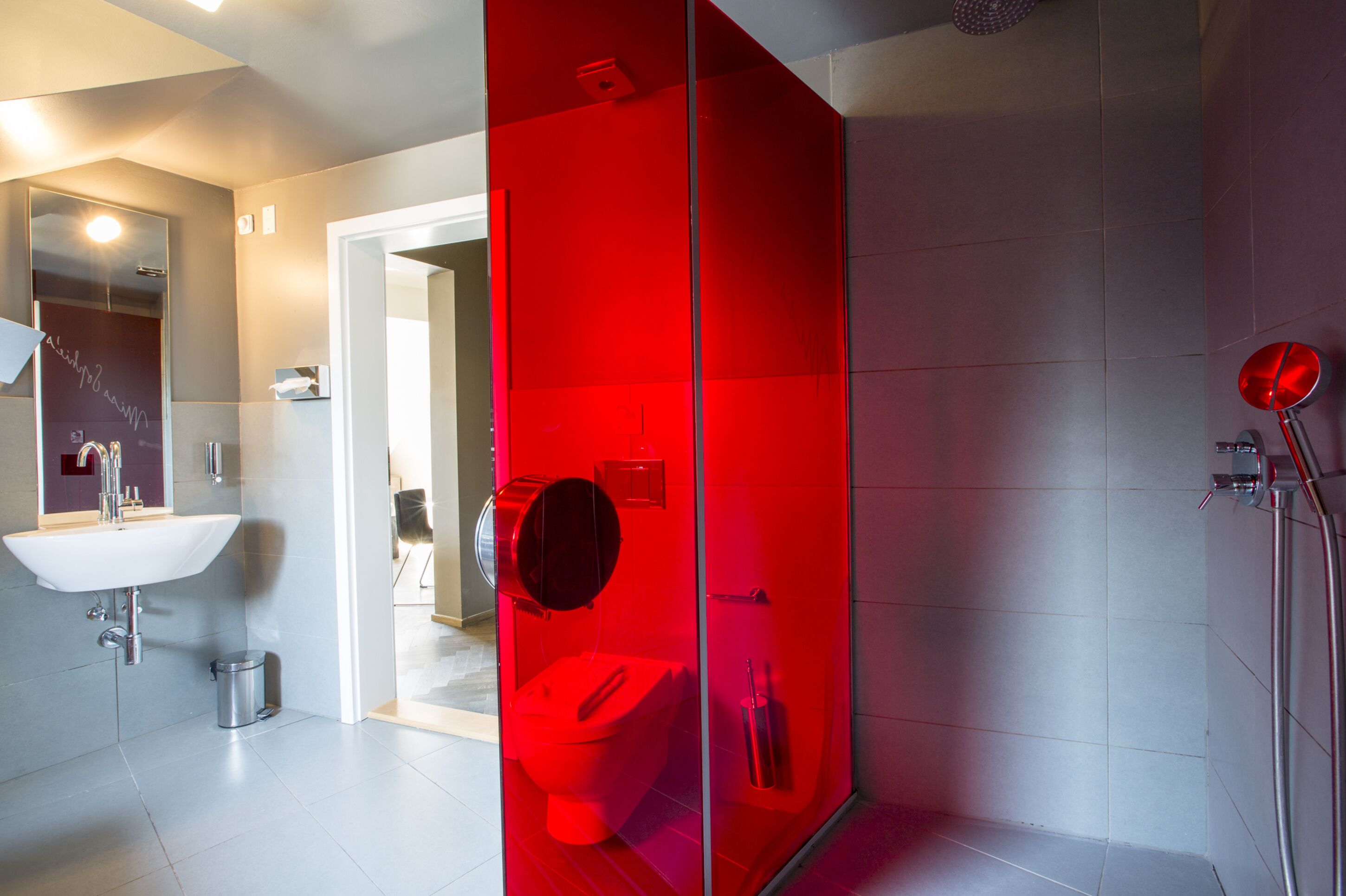 Ein modernes Badezimmer mit einer roten Duschkabine, einem weißen Waschbecken und einer sichtbaren Toilette.