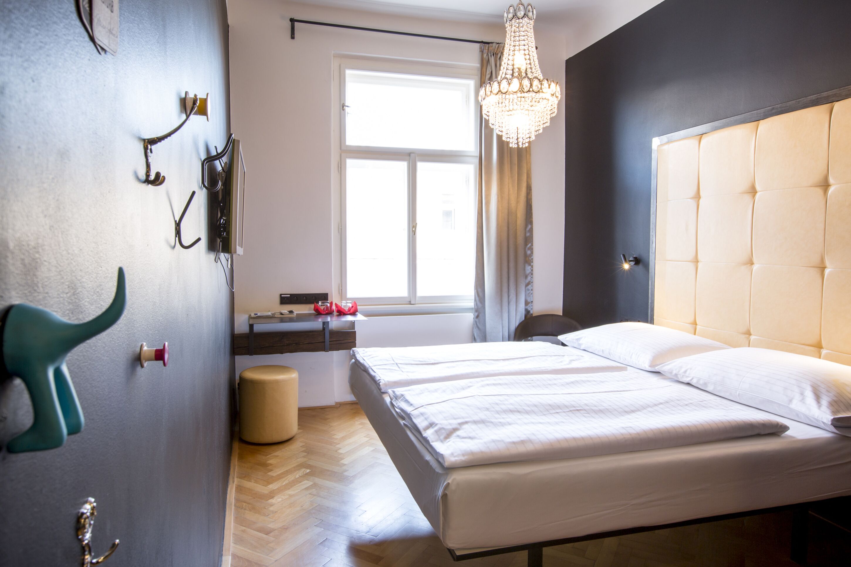 Quarto de hotel com uma cama grande, um candelabro, uma janela com cortinas e piso de madeira.