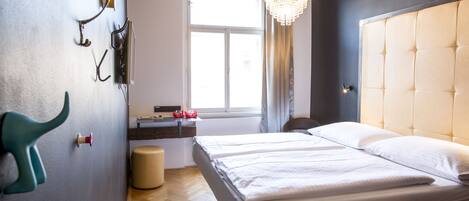 Quarto de hotel com uma cama grande, um candelabro, uma janela com cortinas e piso de madeira.