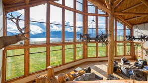 A spacious room with large windows offering a view of a lake and mountains. There are wooden beams on the ceiling and rustic furniture. - Fiordland Lodge (Te Anau)