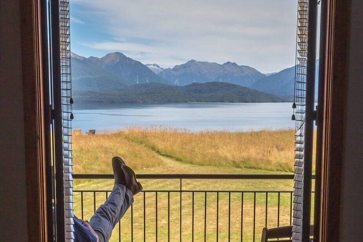 Eine Person entspannt sich auf einem Balkon mit Blick auf einen See und Berge.