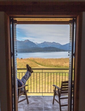Una persona relajándose en un balcón con vista a un lago y montañas.