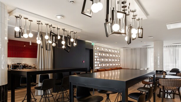 A modern bar area with a long counter, multiple stools, and hanging pendant lights. - ibis Styles Tallinn (Tallinn)
