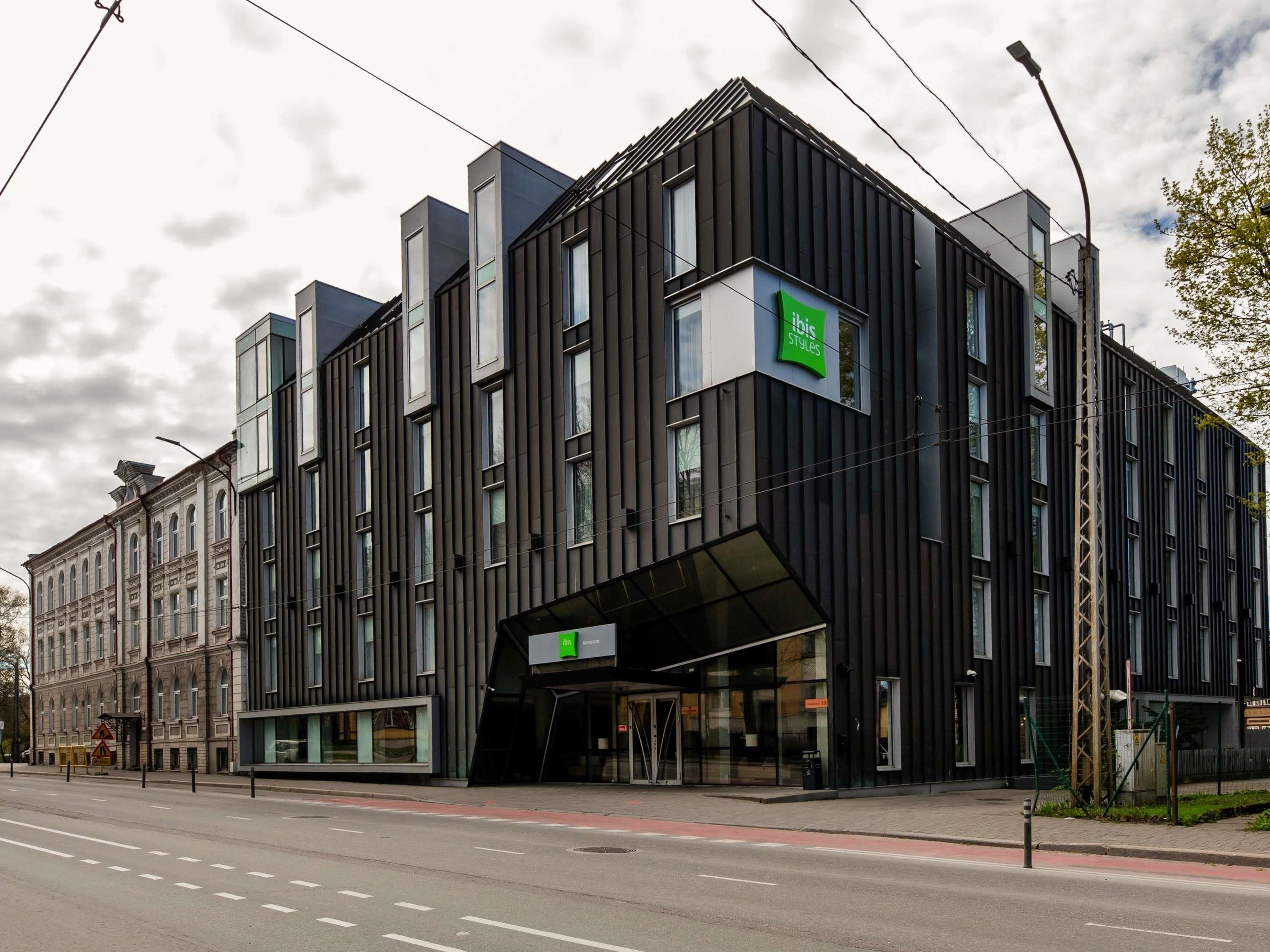 Um edifício moderno com um grande letreiro 'ibis Styles', janelas amplas e entrada coberta.