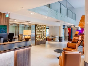 A modern hotel lobby with a reception desk, seating area, and a glass staircase. - ibis Styles Tallinn (Tallinn)