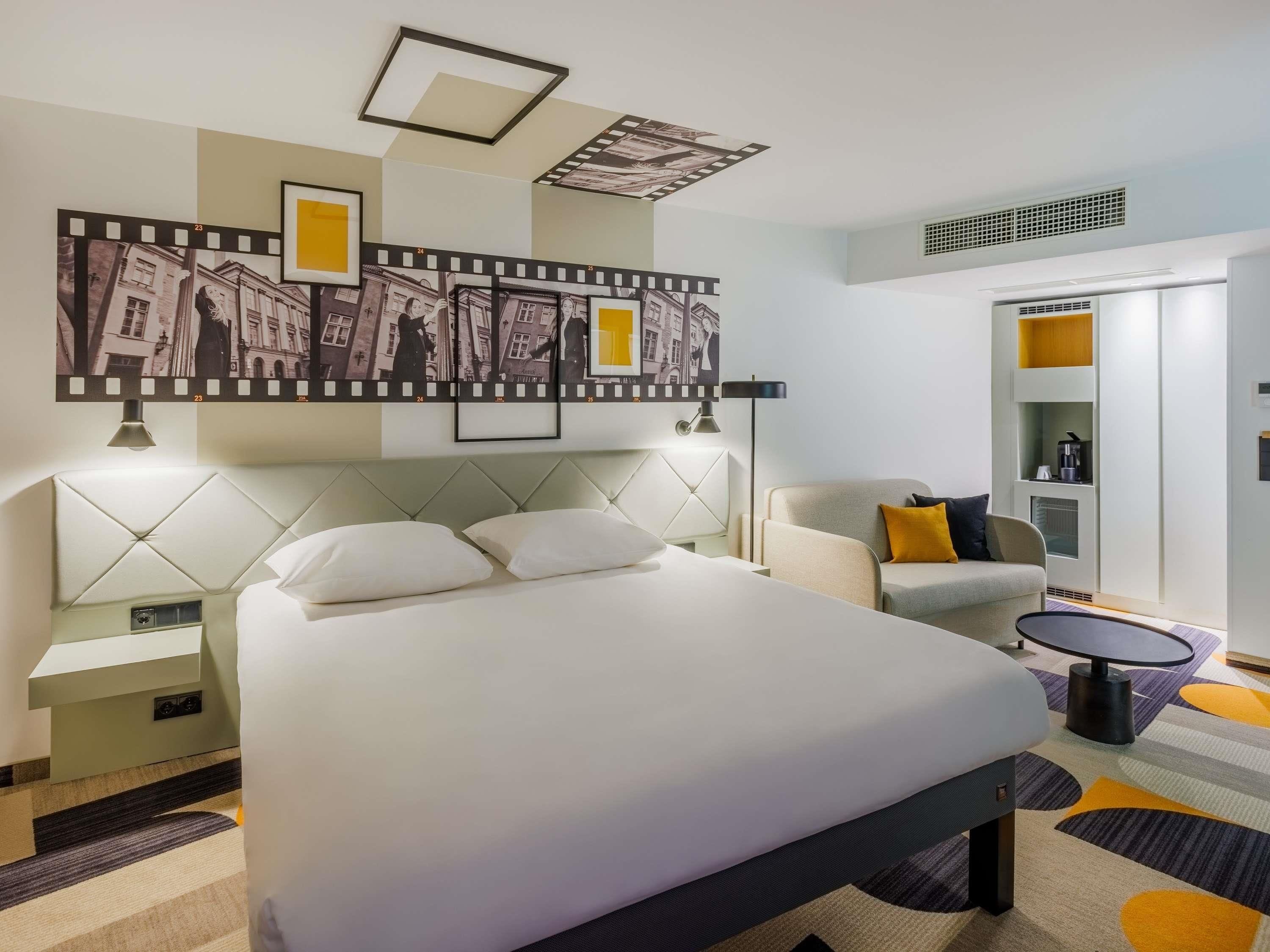Een hotelkamer met een bed, een slaapbank, een kleine tafel, een lamp, een wandplank en een plafondlamp.