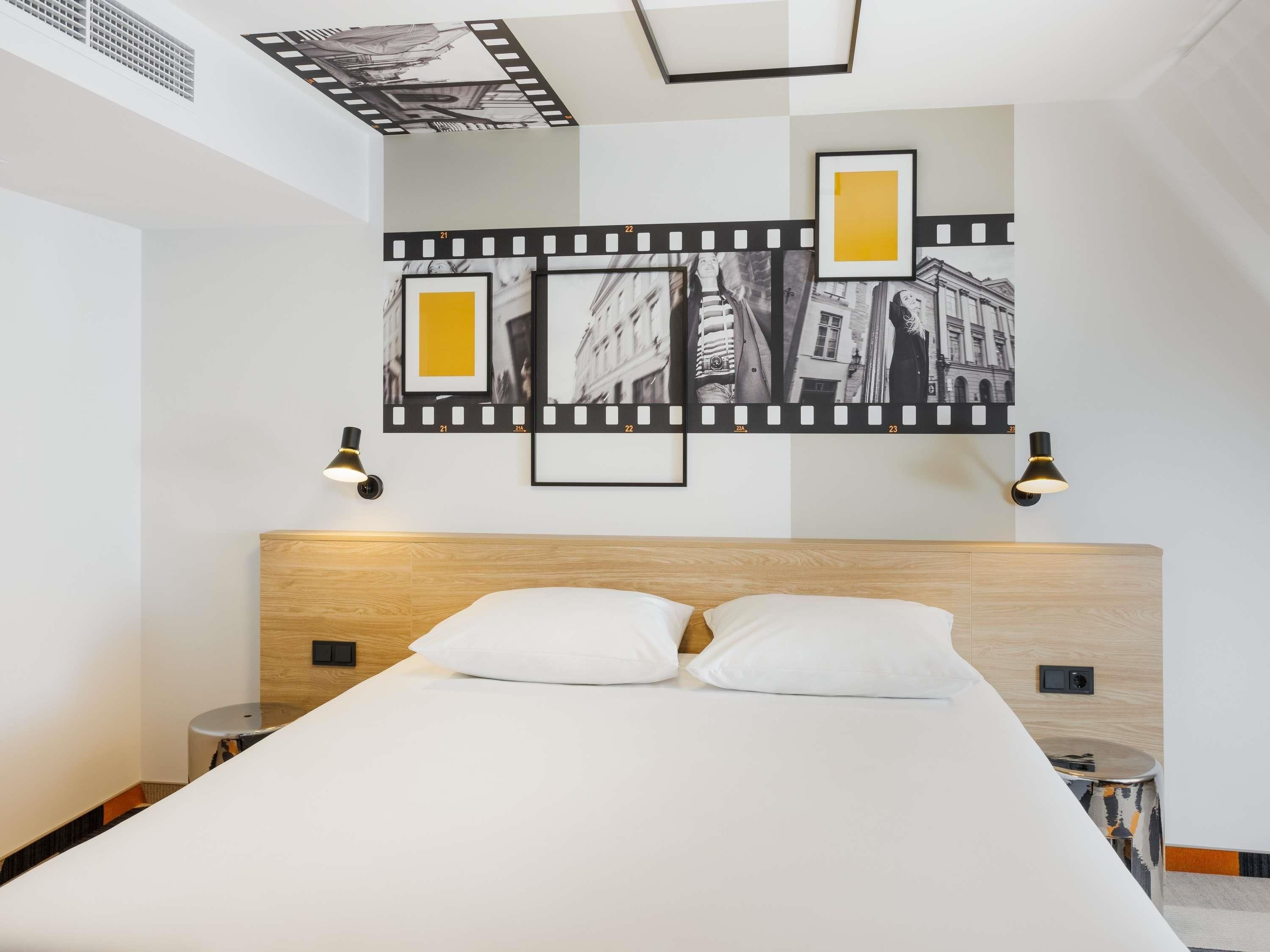 A modern hotel room with a large bed, two bedside tables, and a wall-mounted filmstrip artwork.