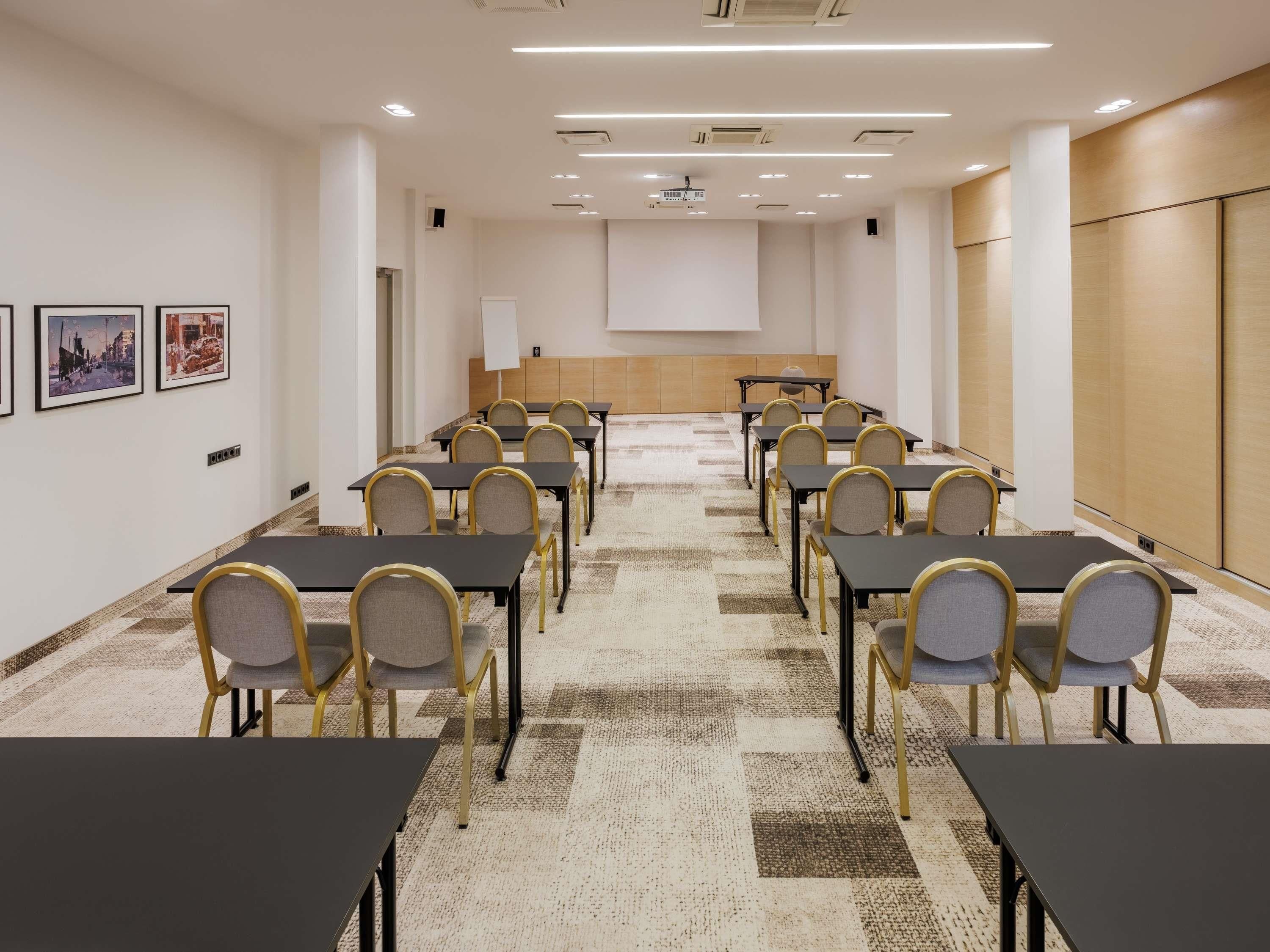 A conference room with tables and chairs arranged for meetings, a projector screen, and a carpeted floor.