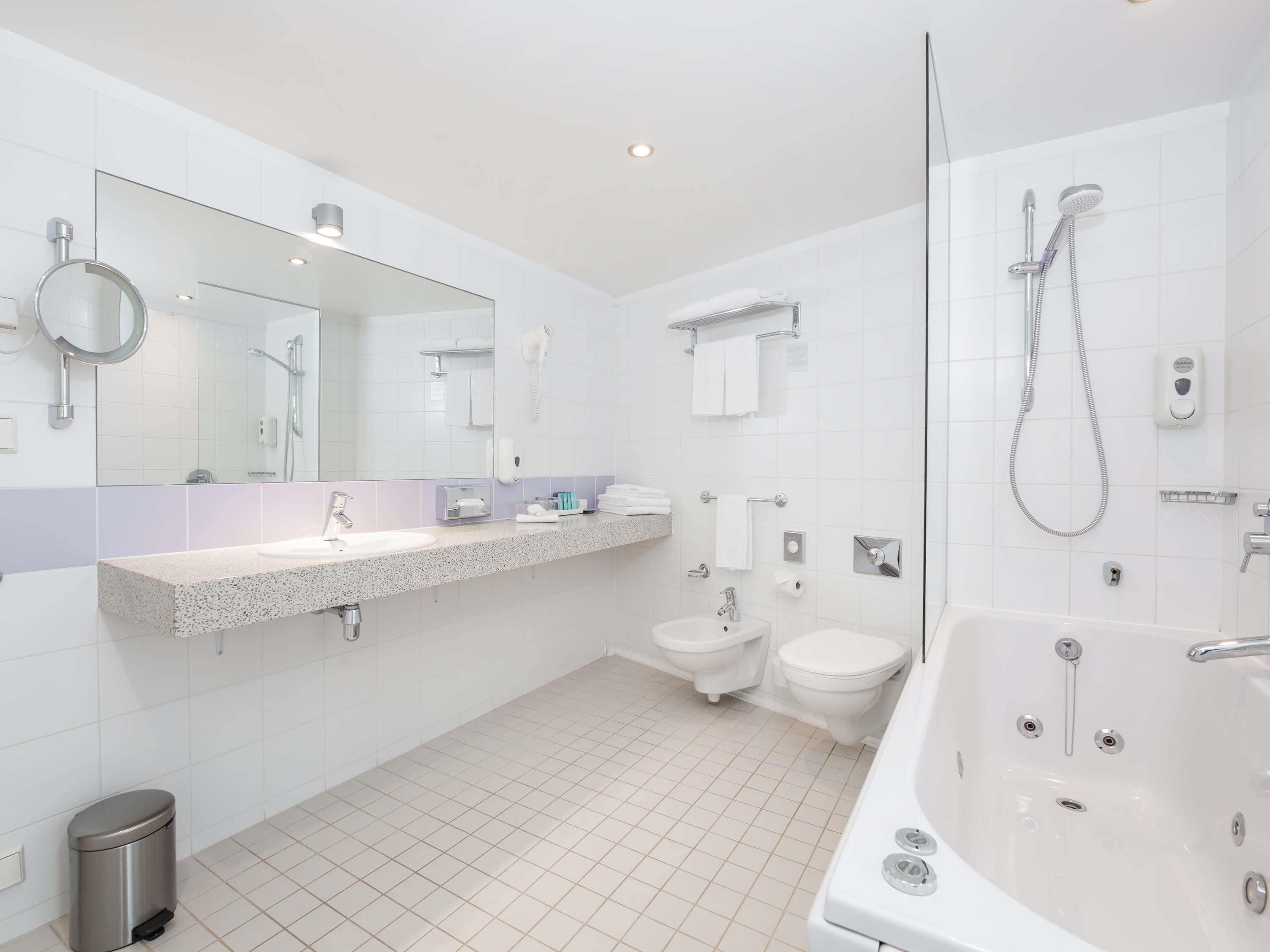 A modern bathroom with a large mirror, a sink, a toilet, a shower, and a bathtub.