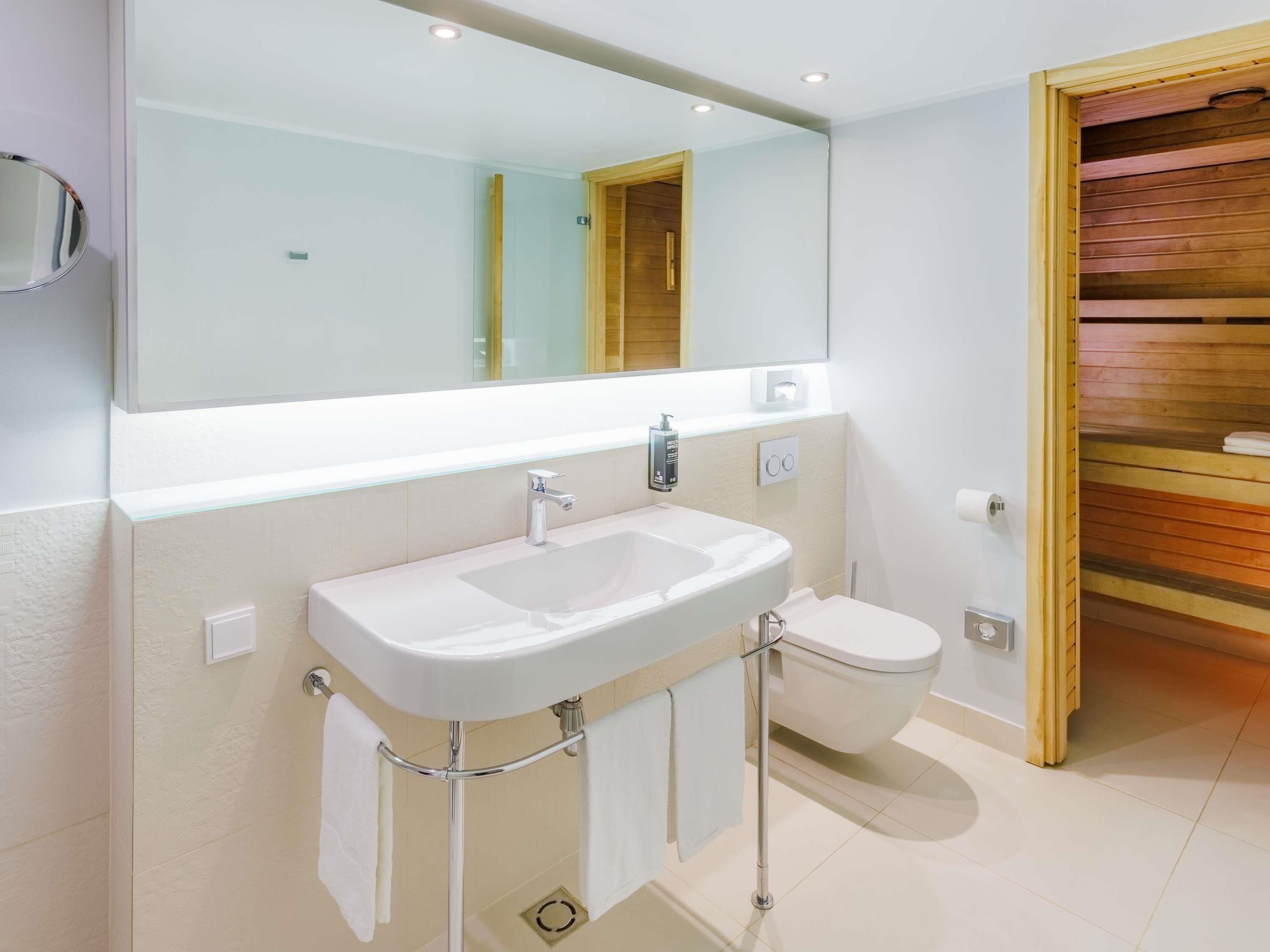 Un baño moderno con lavamanos, espejo y retrete blancos.