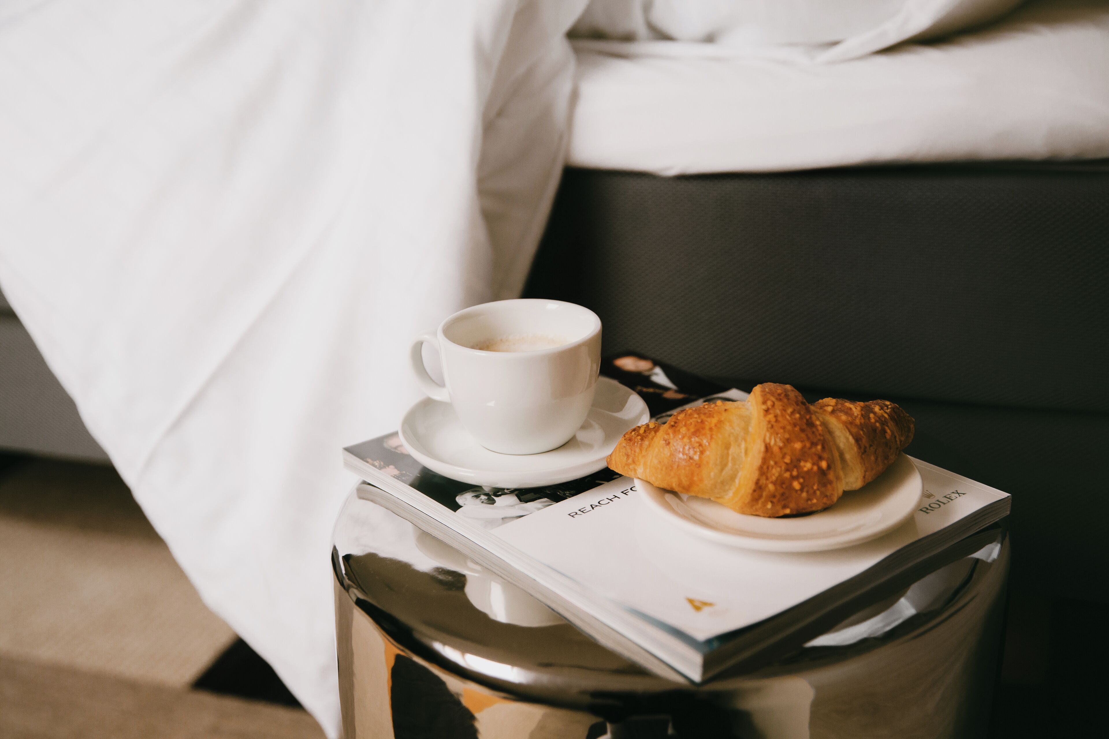 Tarjottimella on croissant ja kuppi kahvia, ja sen päällä on lehti.