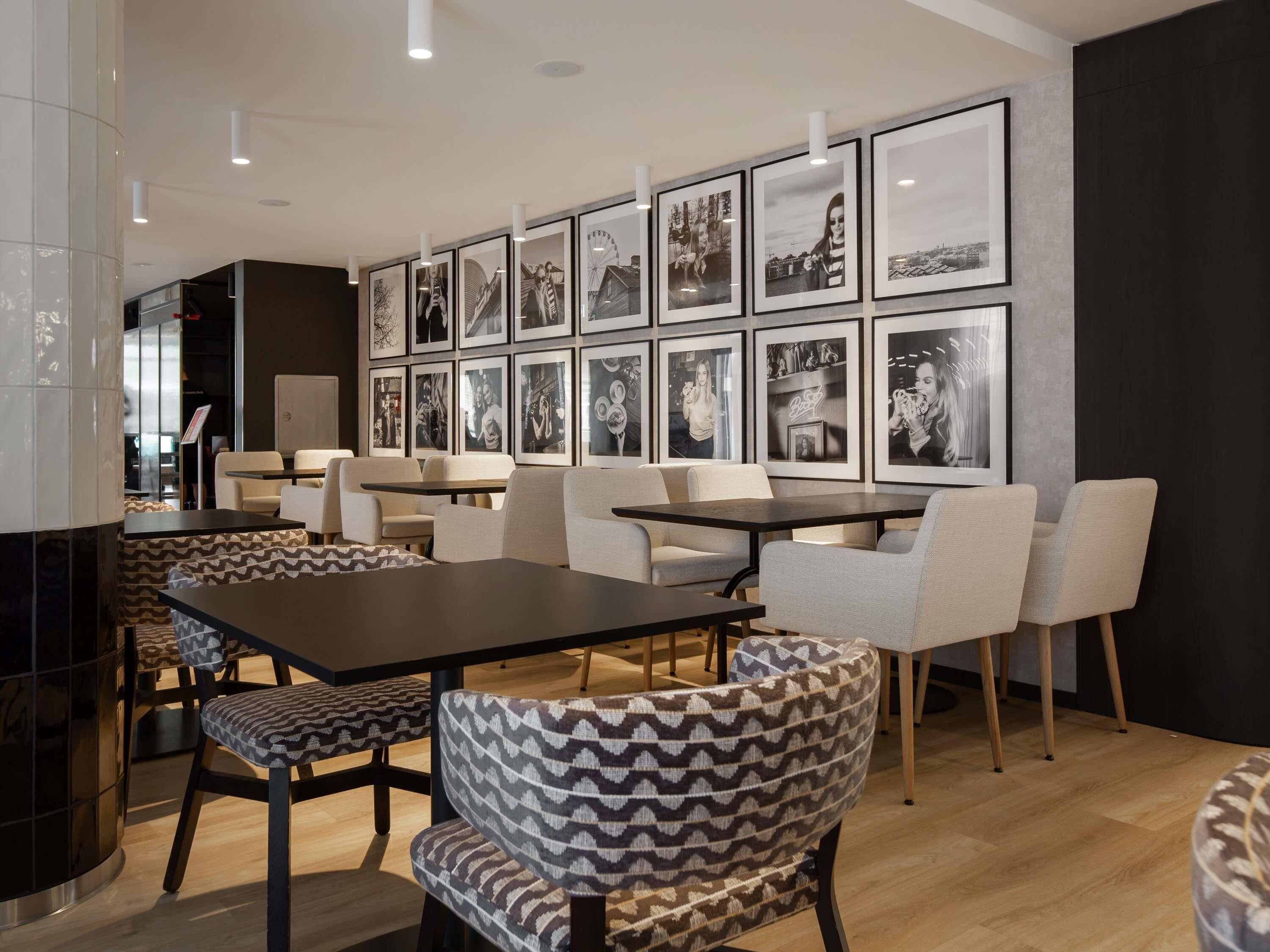 Un café moderne doté de plusieurs espaces de détente, comprenant des tables et des chaises, et dont un mur est décoré de photographies en noir et blanc encadrées.