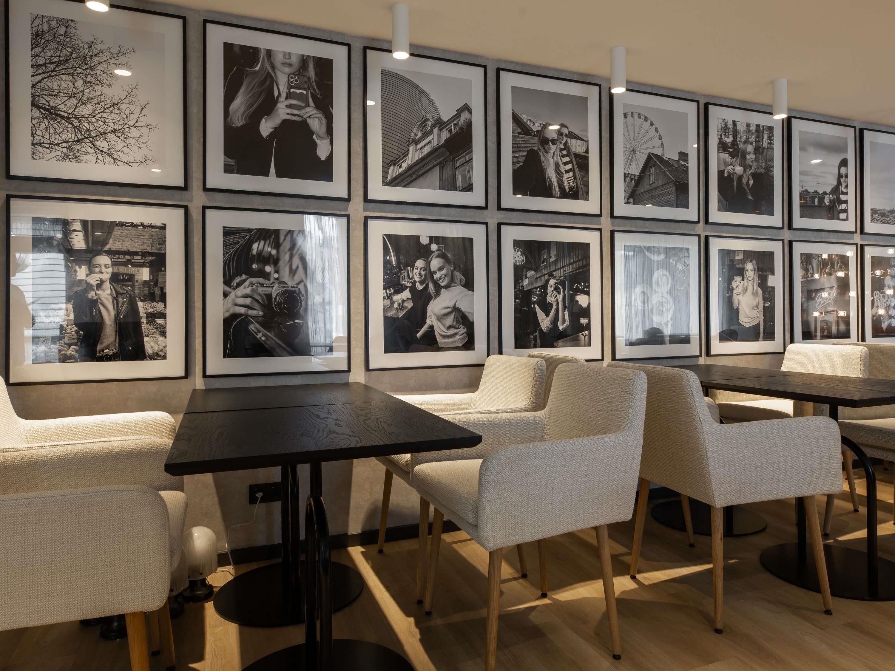 Ein modernes Interieur mit gerahmten Schwarz-Weiß-Fotografien an der Wand, einem dunklen Holztisch und hellen gewebten Stühlen.