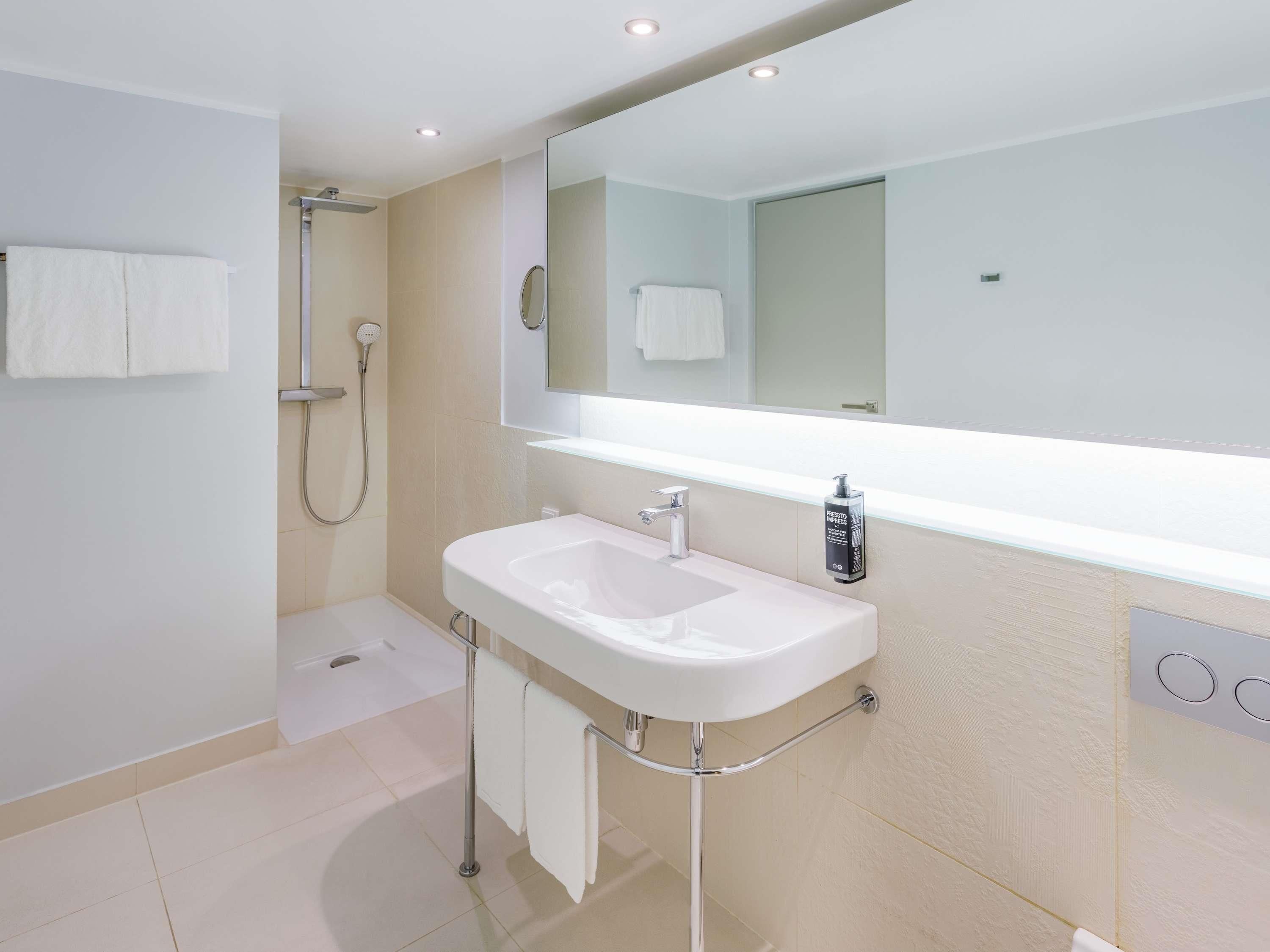 Un bagno moderno con un lavandino bianco, un ampio specchio e una doccia.
