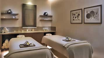 Relax in a serene spa room with two treatment beds, a flower arrangement, and calming botanical prints.