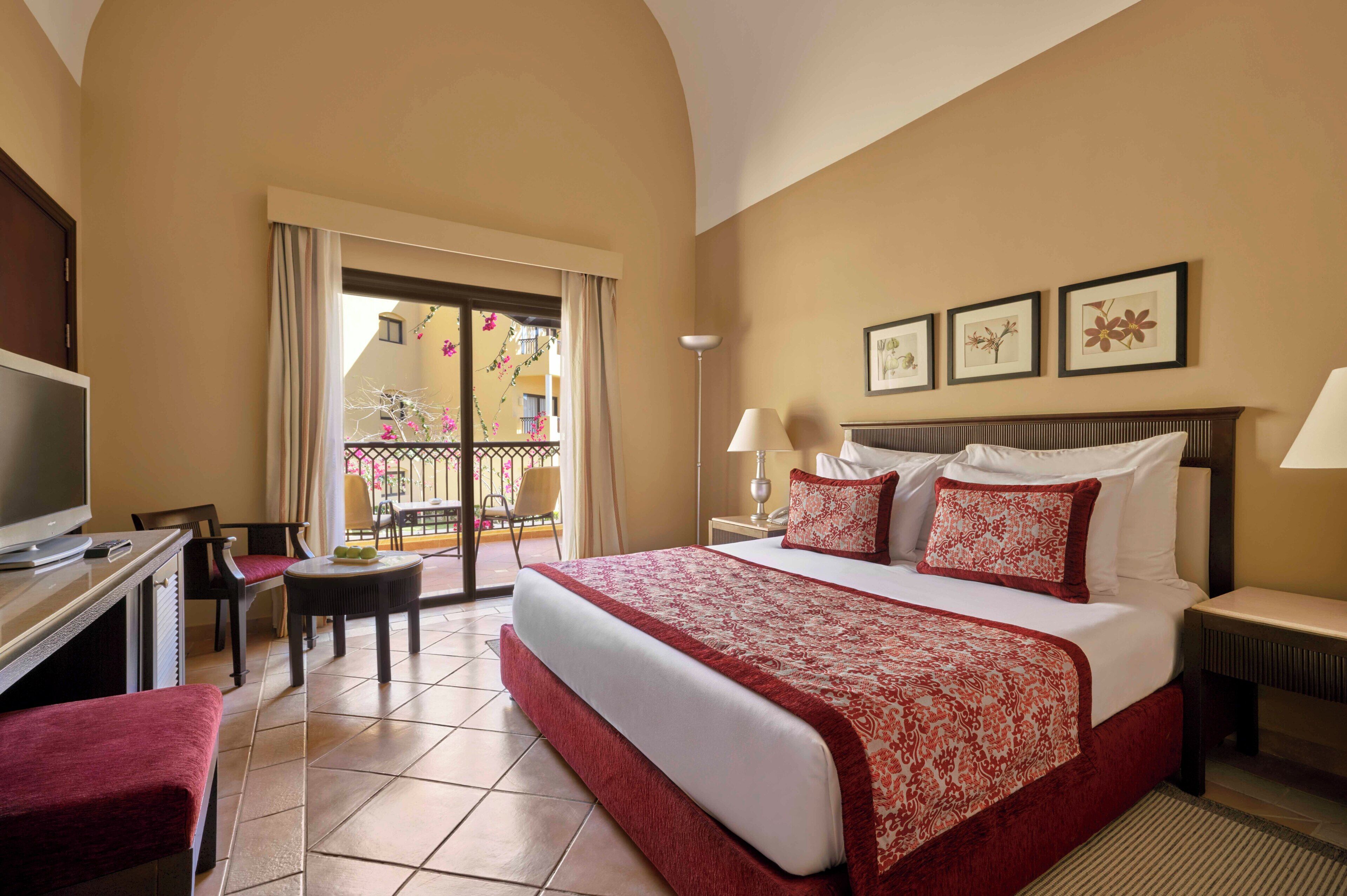 A hotel room with a bed, a desk, a chair, a TV, and a balcony with a view.