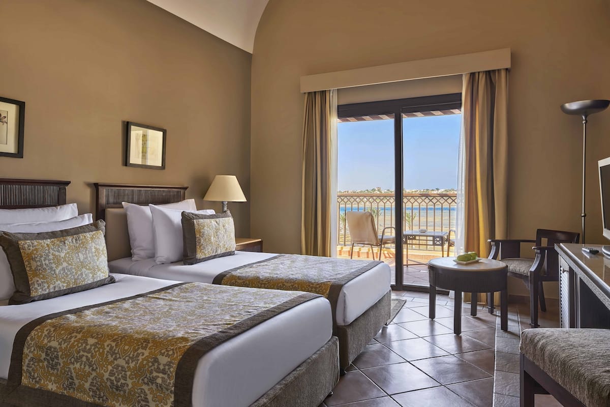 A hotel room with two beds, a TV, a balcony with a view, and a dining area.