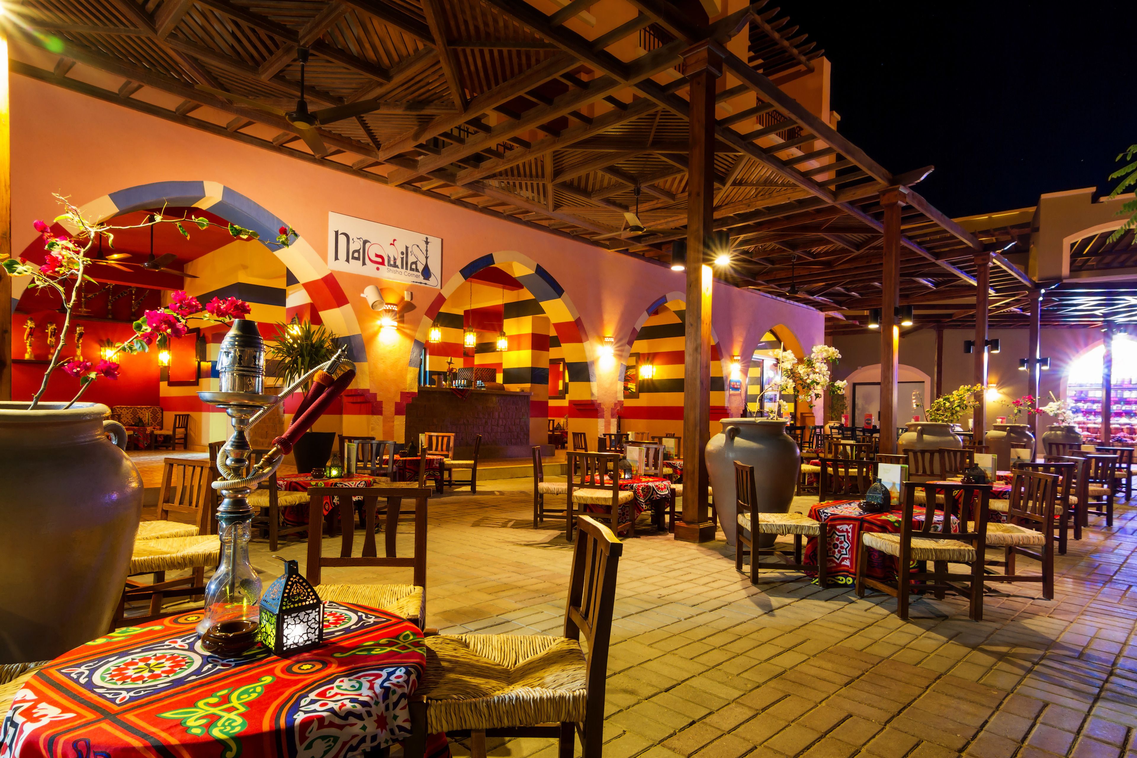 An outdoor restaurant with wooden tables and chairs, a large decorative vase, and a sign reading "nagaraja".