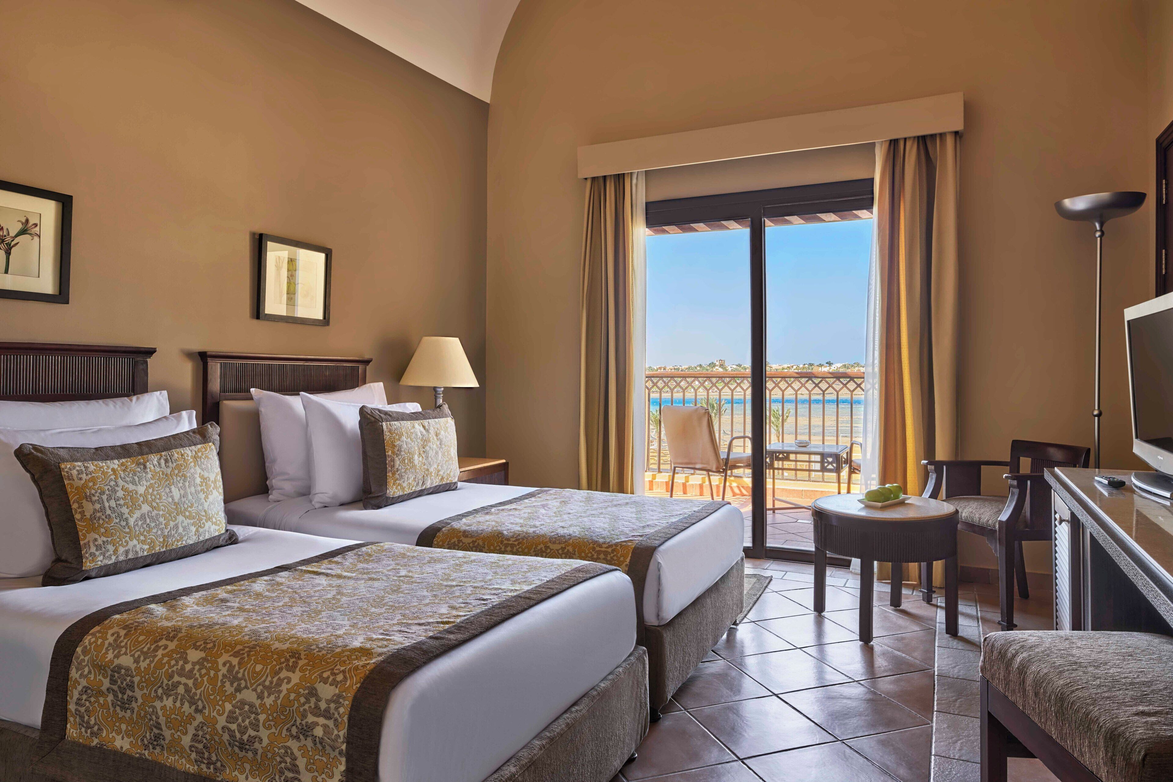 A hotel room with two beds, a TV, a balcony with a view, and a dining area.