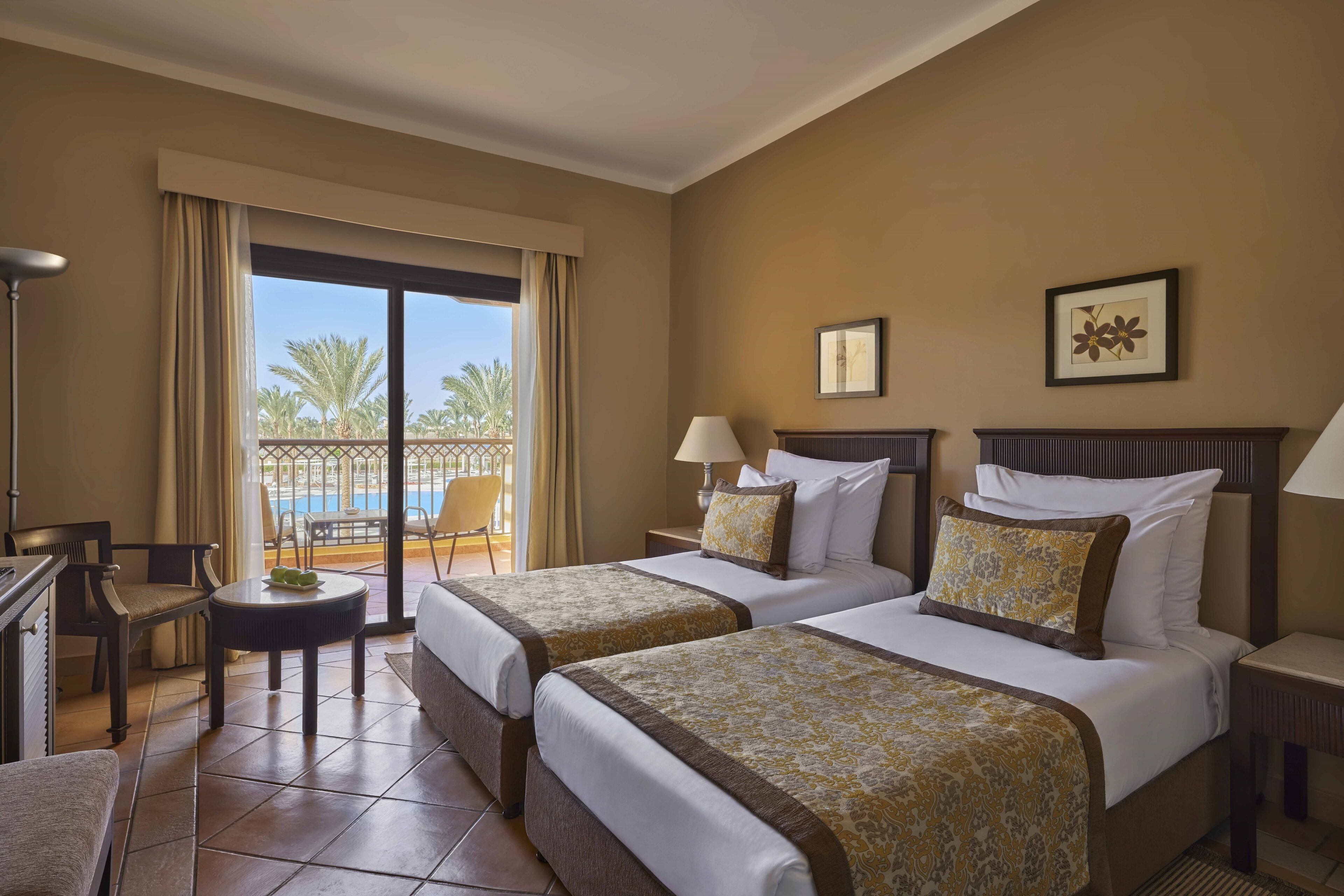 Une chambre d’hôtel avec deux lits, un bureau, une chaise et un balcon donnant sur la piscine.