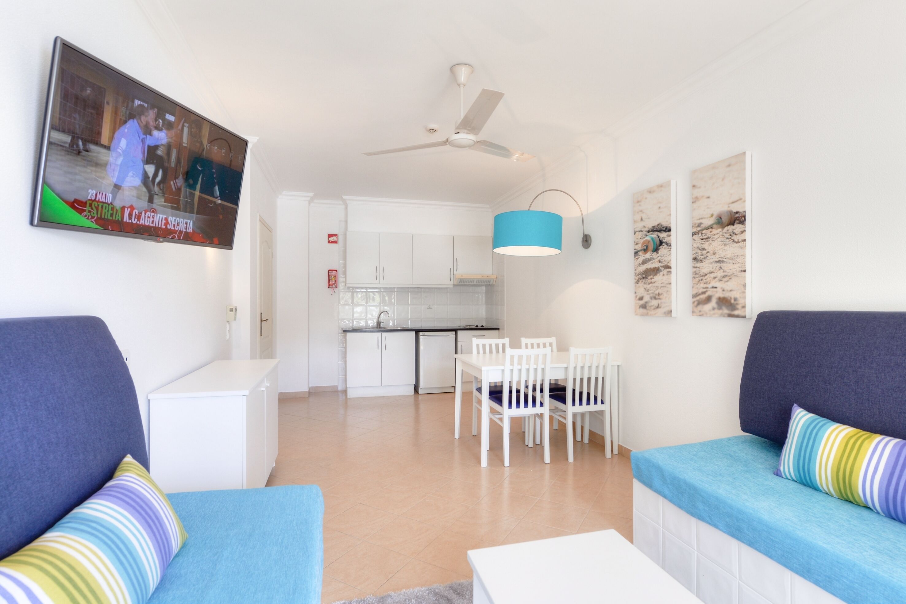 Een moderne woonkamer met een televisie, bank, eettafel en keuken op de achtergrond.