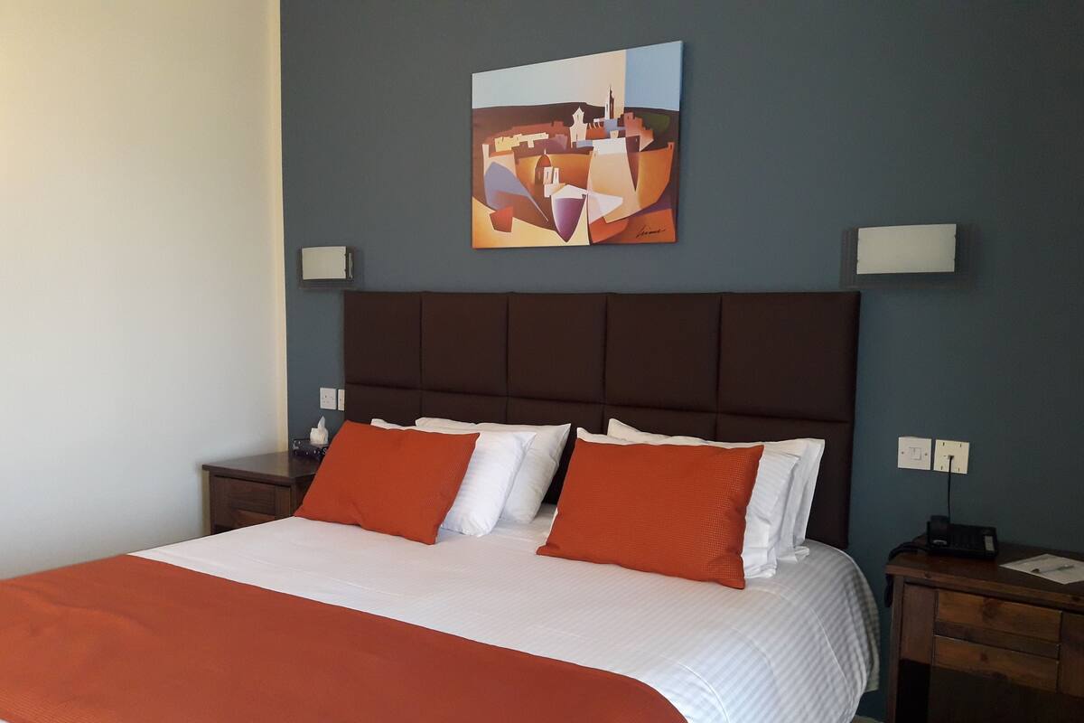 A hotel room with a large bed, two nightstands, a headboard, and a painting on the wall.