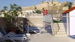 Une terrasse sur le toit, avec des chaises longues, un escalier et une vue sur un bâtiment historique en arrière-plan.