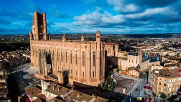 A large, historic building with multiple towers and a prominent central tower, surrounded by a densely built urban area.
