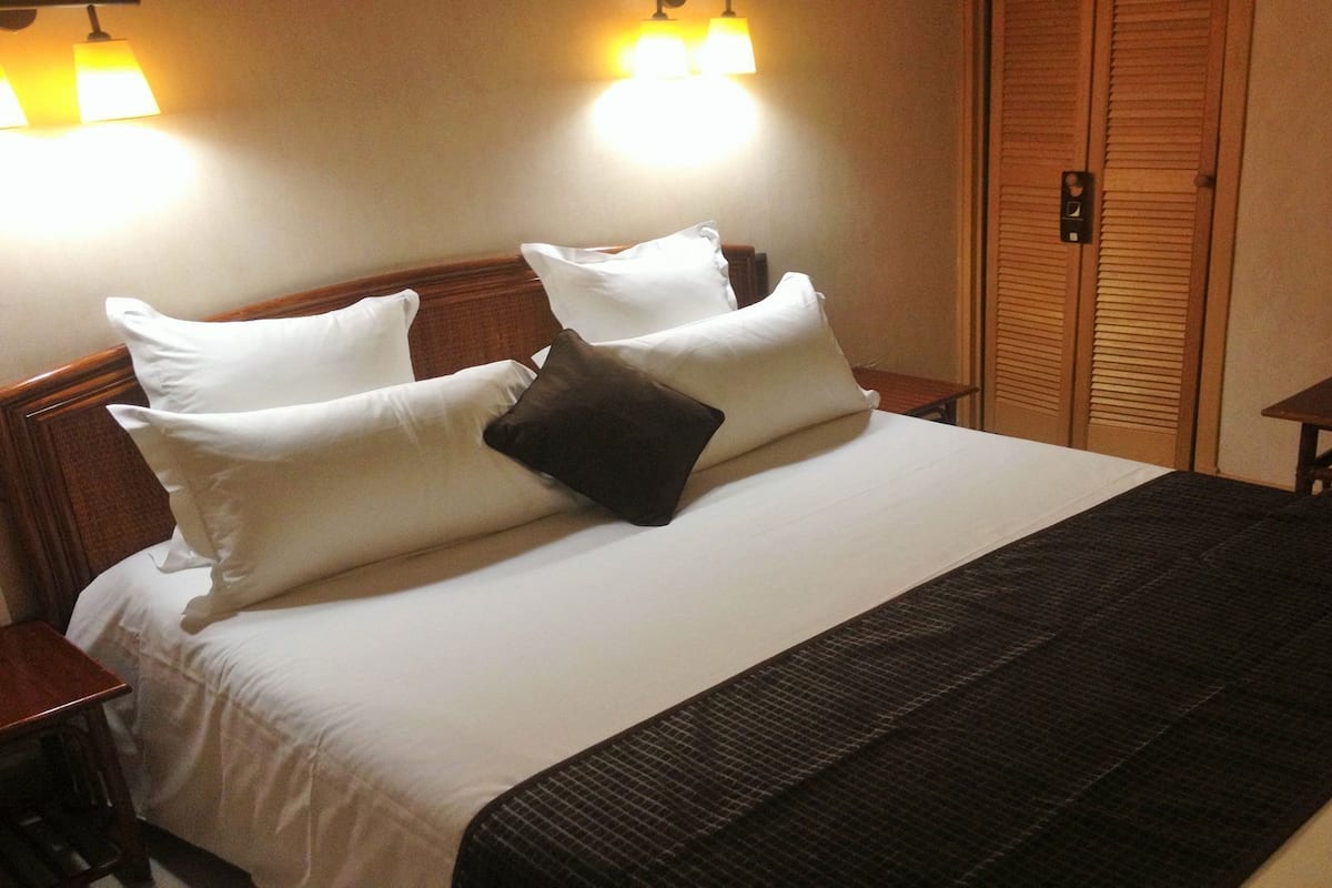A hotel room with a large bed, two bedside tables, a wooden wardrobe, and two wall-mounted lamps.