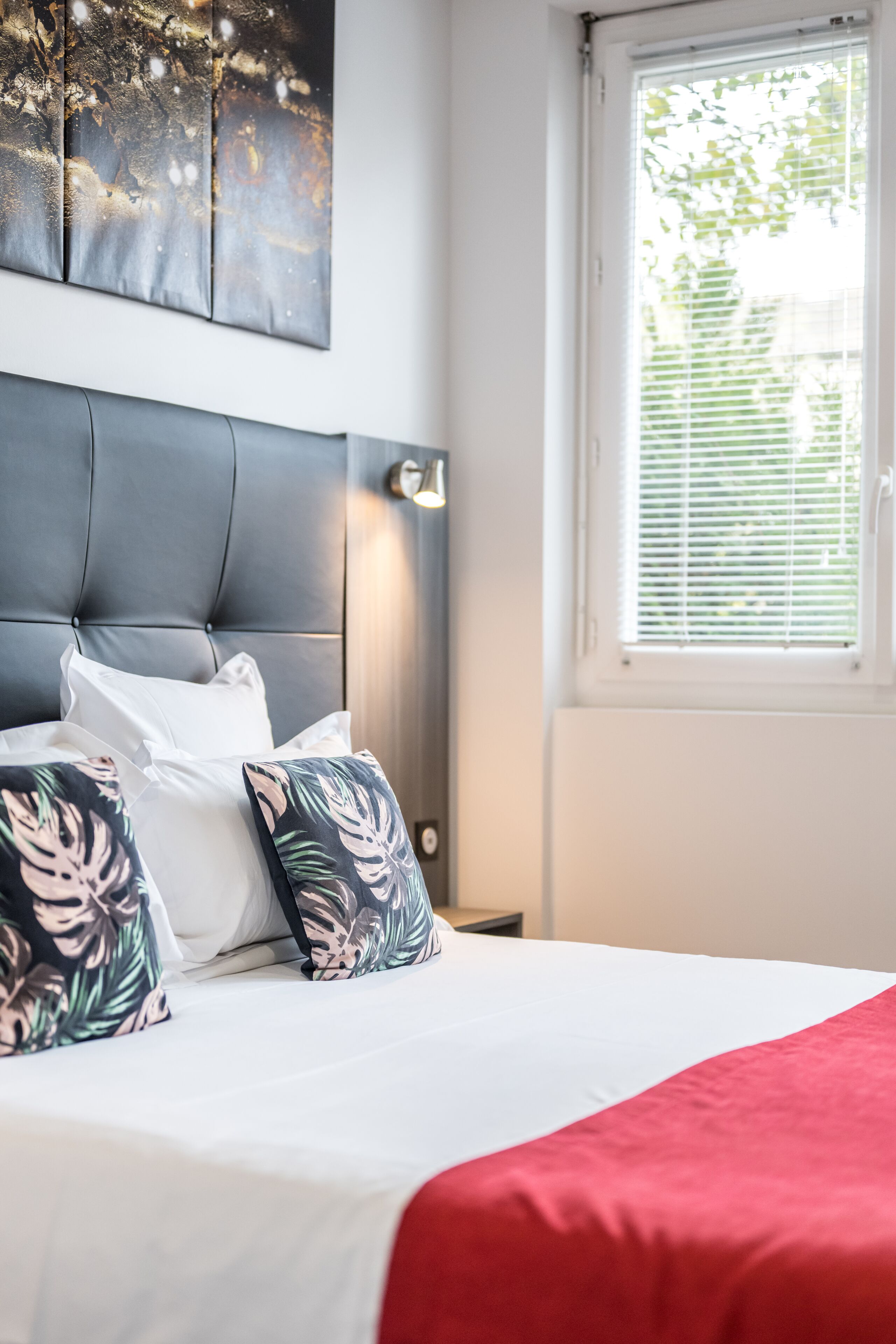 A neatly made bed with a red blanket, white pillows, and a floral pillow.