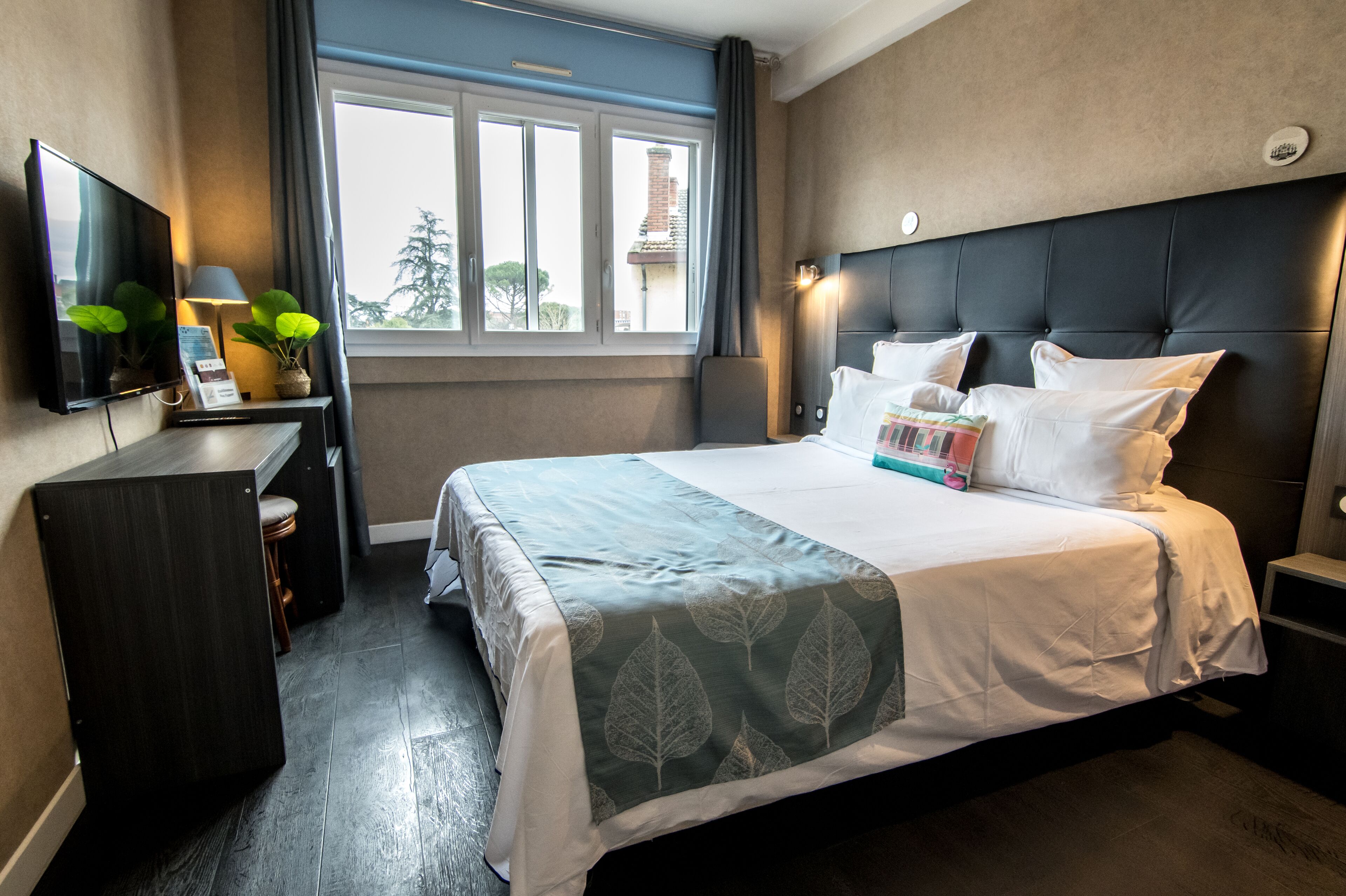 A hotel room with a bed, a desk, a TV, and a window with curtains.