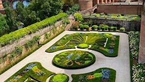 Ein formaler Garten mit geometrischen Mustern, einer Brücke und einem historischen Gebäude im Hintergrund.