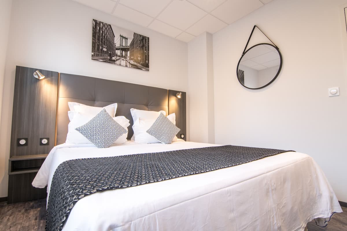 A neatly made bed with a patterned bedspread, a headboard with built-in lighting, and a wall-mounted mirror.