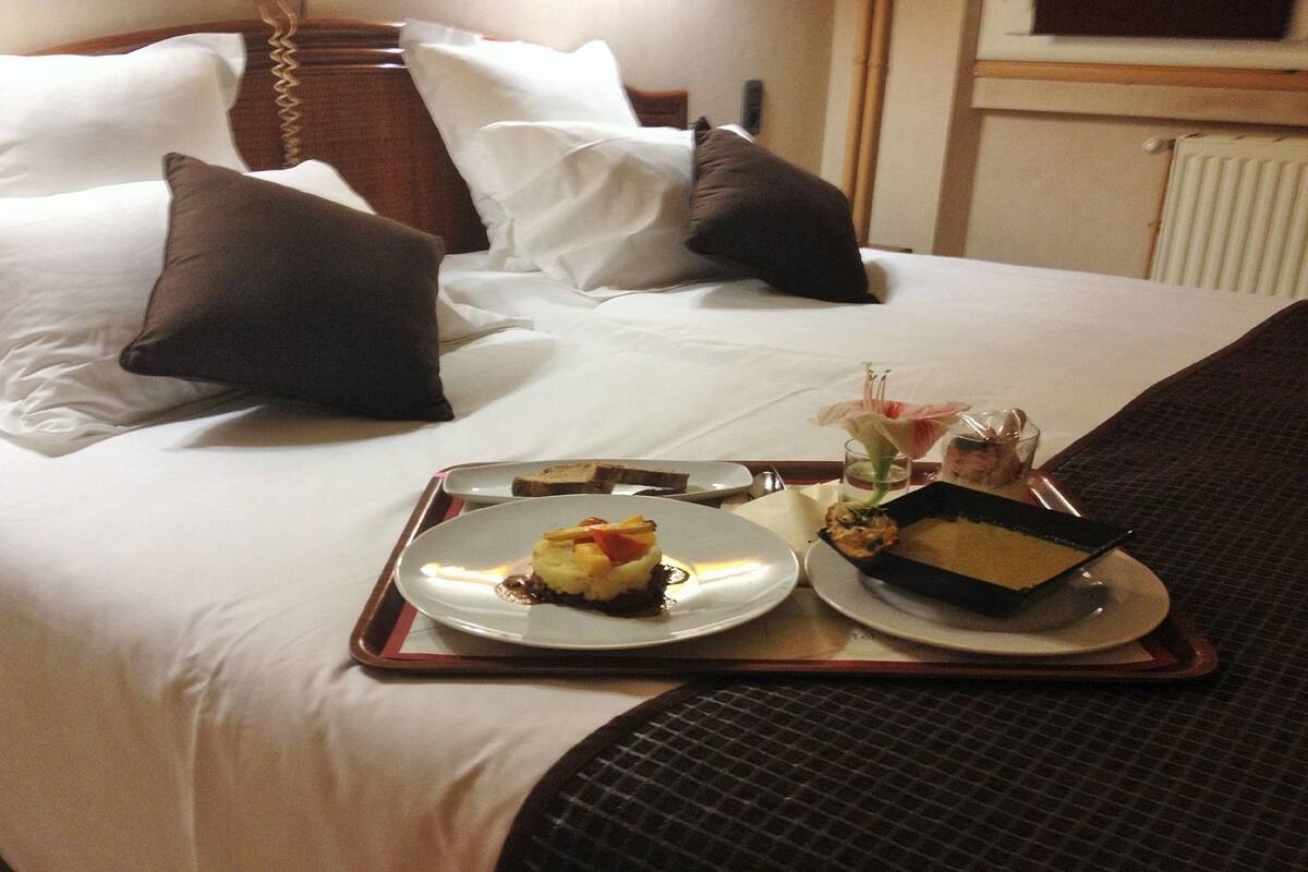 A neatly made bed with white and brown pillows, a tray with two plates of food, and a vase with flowers.