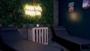 Eine Lounge-Ecke mit zwei Liegesesseln, einem Neon-Schild mit der Aufschrift 'happy wife, happy life', einer Ziegelwand mit Grünpflanzen und einem gerahmten Bild.