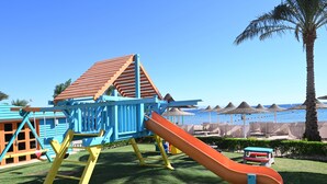 Ein Spielplatz mit Rutsche und Klettergerüst vor einer Strandkulisse.