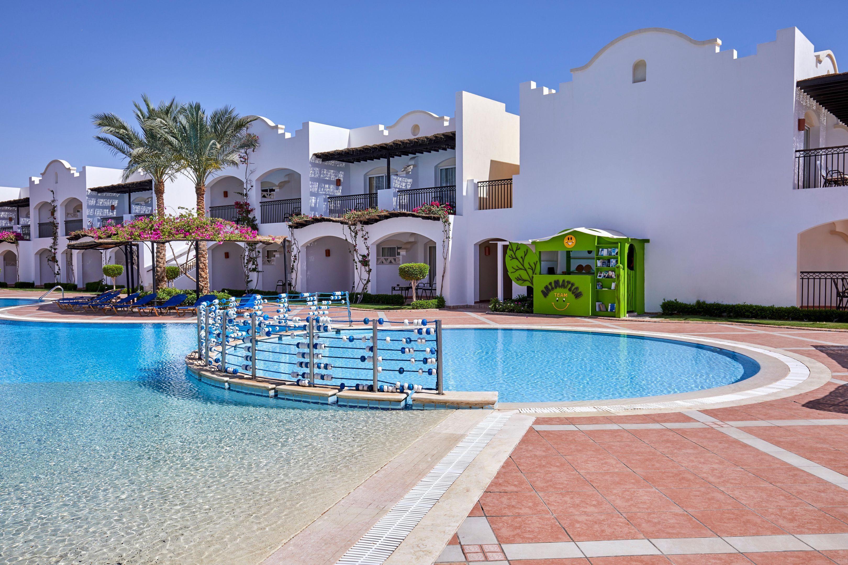 A swimming pool with a water slide, palm trees, and a building with balconies.