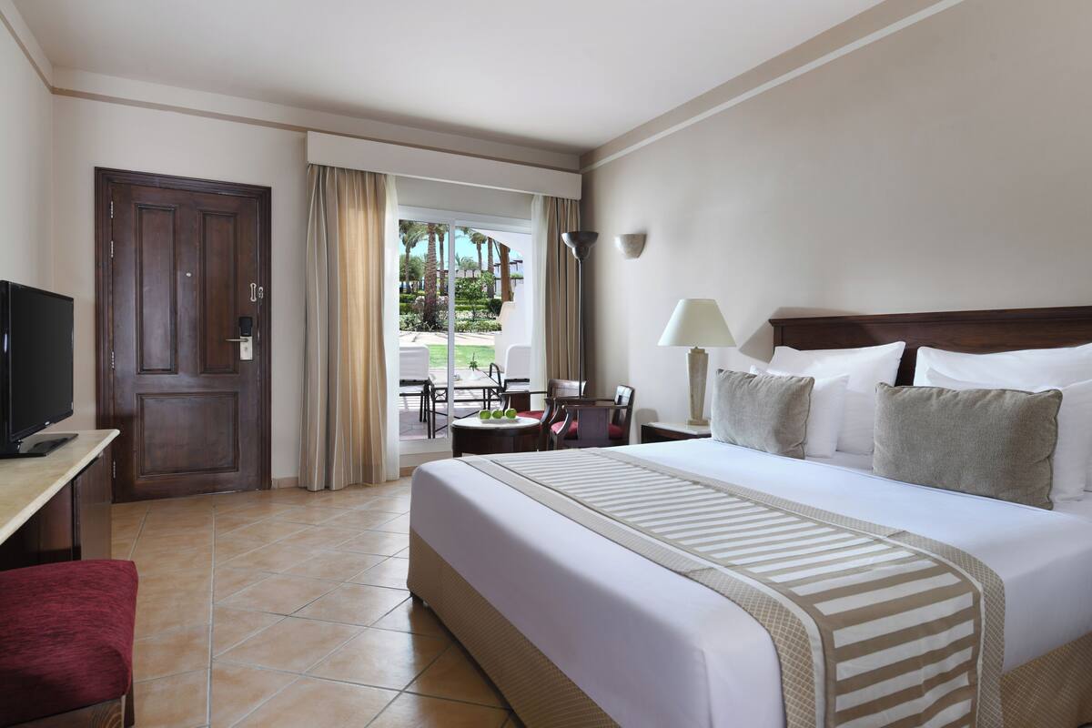 A hotel room with a large bed, a desk with a TV, a chair, and a view of the outdoors.